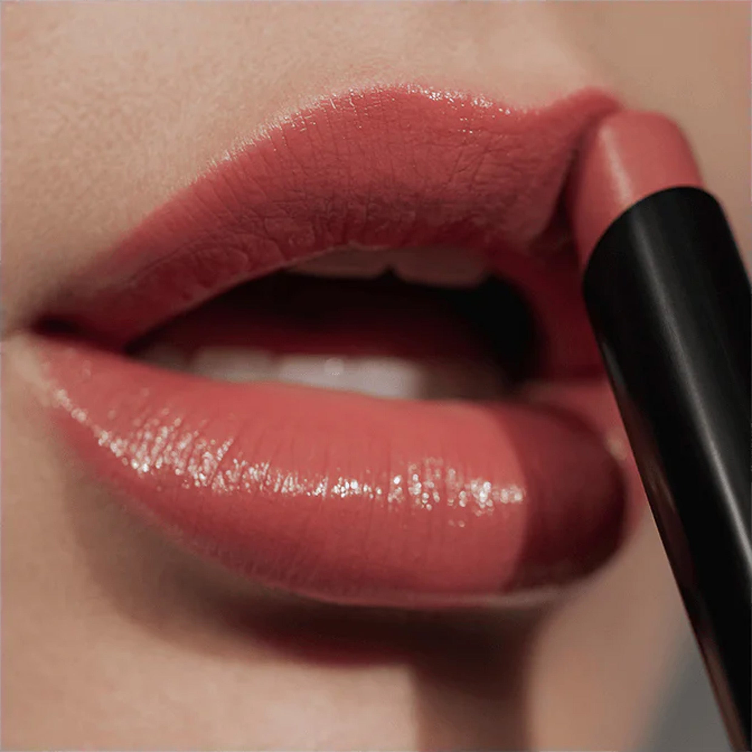 A close up image of lips with a lipstick being applied in a warm rose colour.