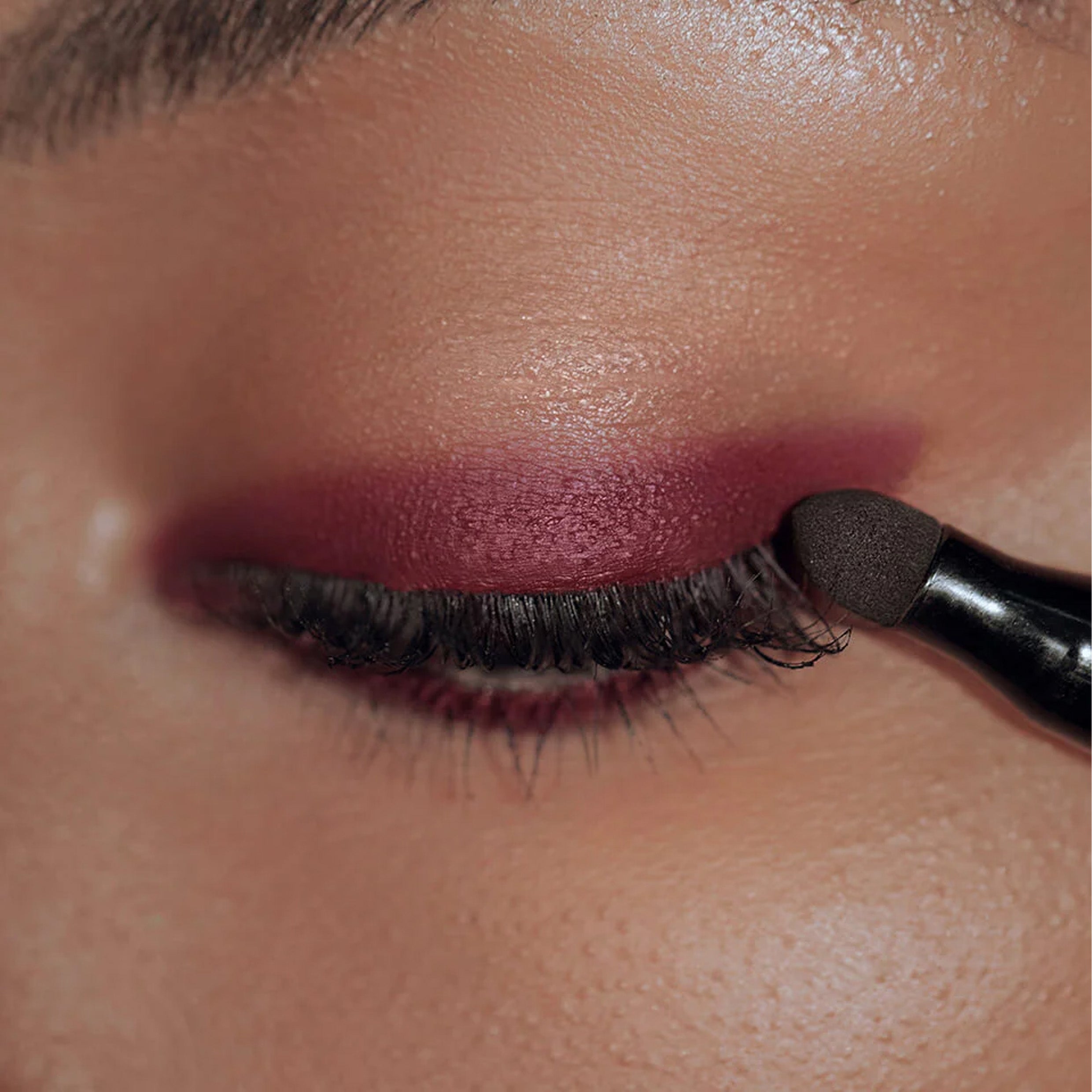 A close up image of eye lid with maroon coloured eyeliner being applied.