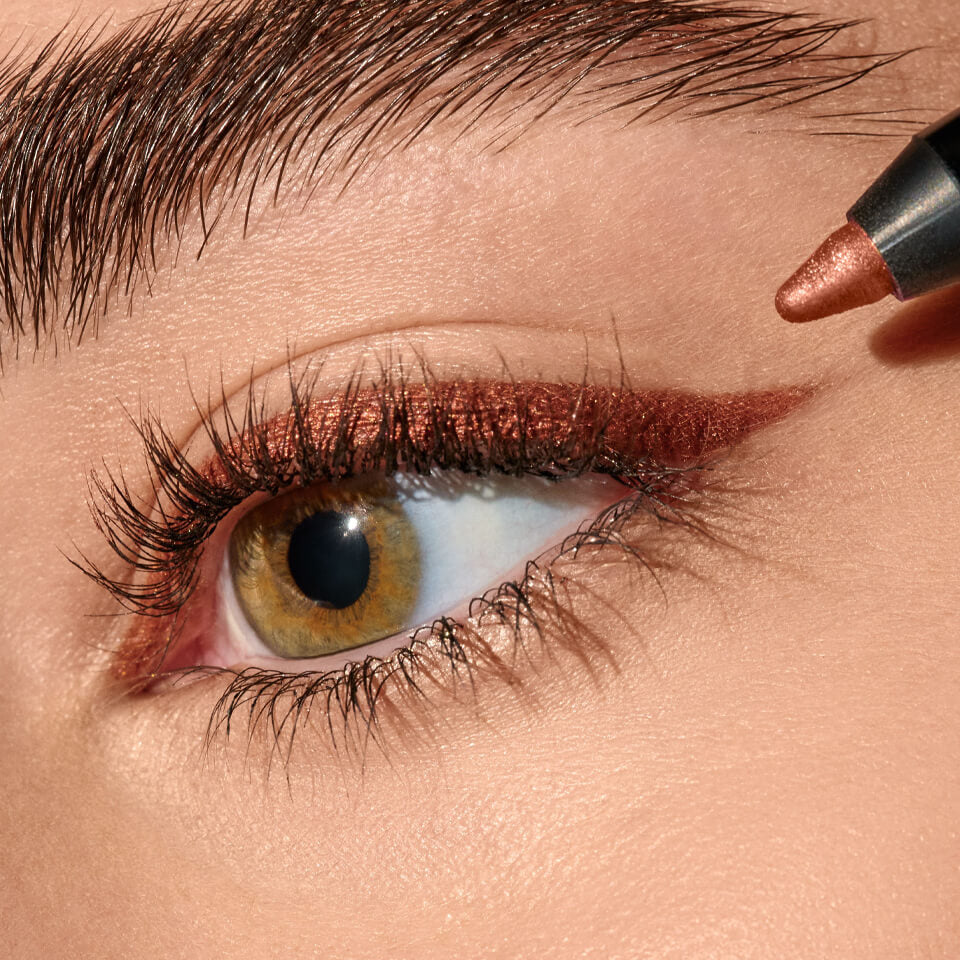 A close up image of an eye with a copper shaded eyeliner being applied to the eyelid.