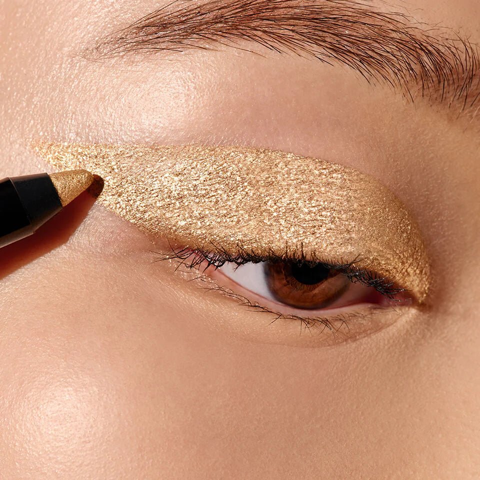 A close up image of an eye with gold eyeliner applied to the eyelid.