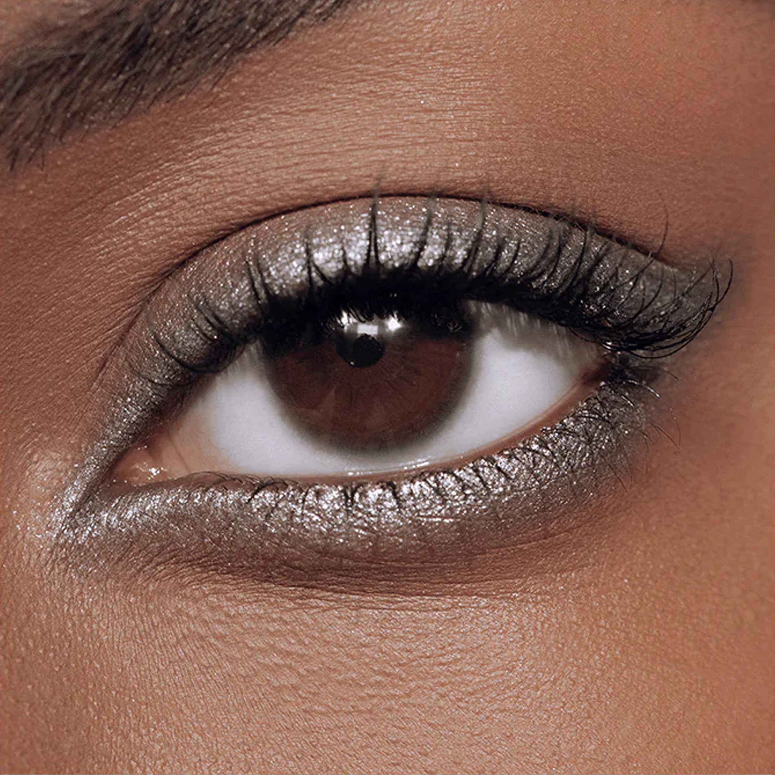 A close up image of an open eye with a shimmery grey eye liner on the eyelid.