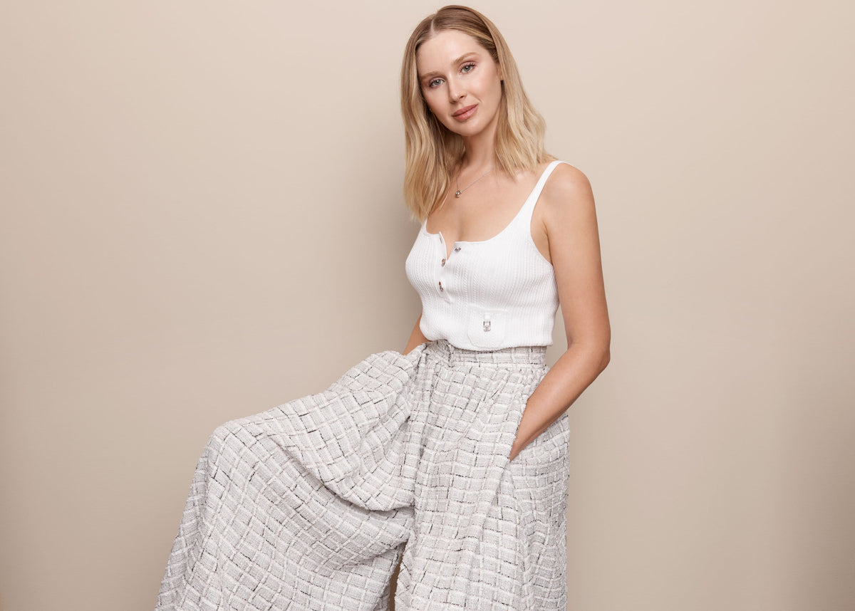 Melanie Grant in a white sleeveless top and wide-leg trousers against a beige backdrop.
