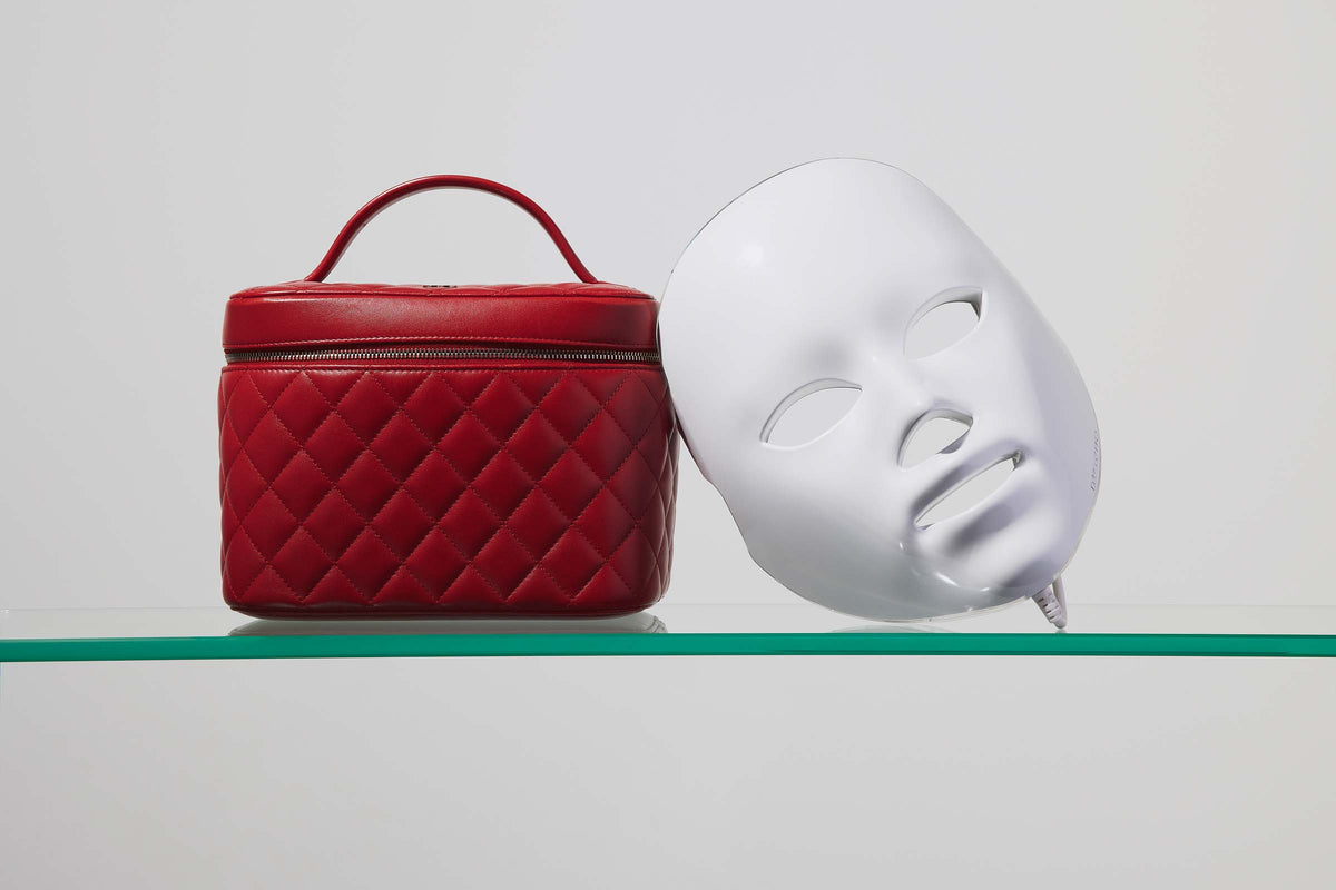 A white Déesse LED mask alongside a red case on a glass shelf