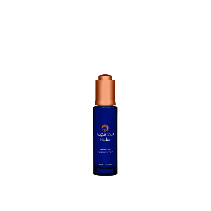 A bottle of Augustinus Bader The Face Oil with a dark blue label and copper-colored cap.
