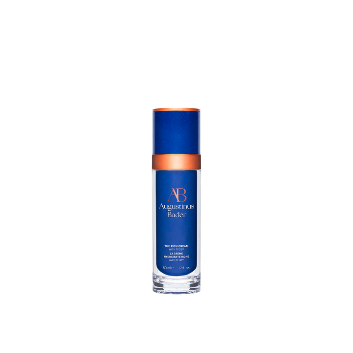 A blue and white bottle of Augustinus Bader The Rich Cream with a copper-colored cap.