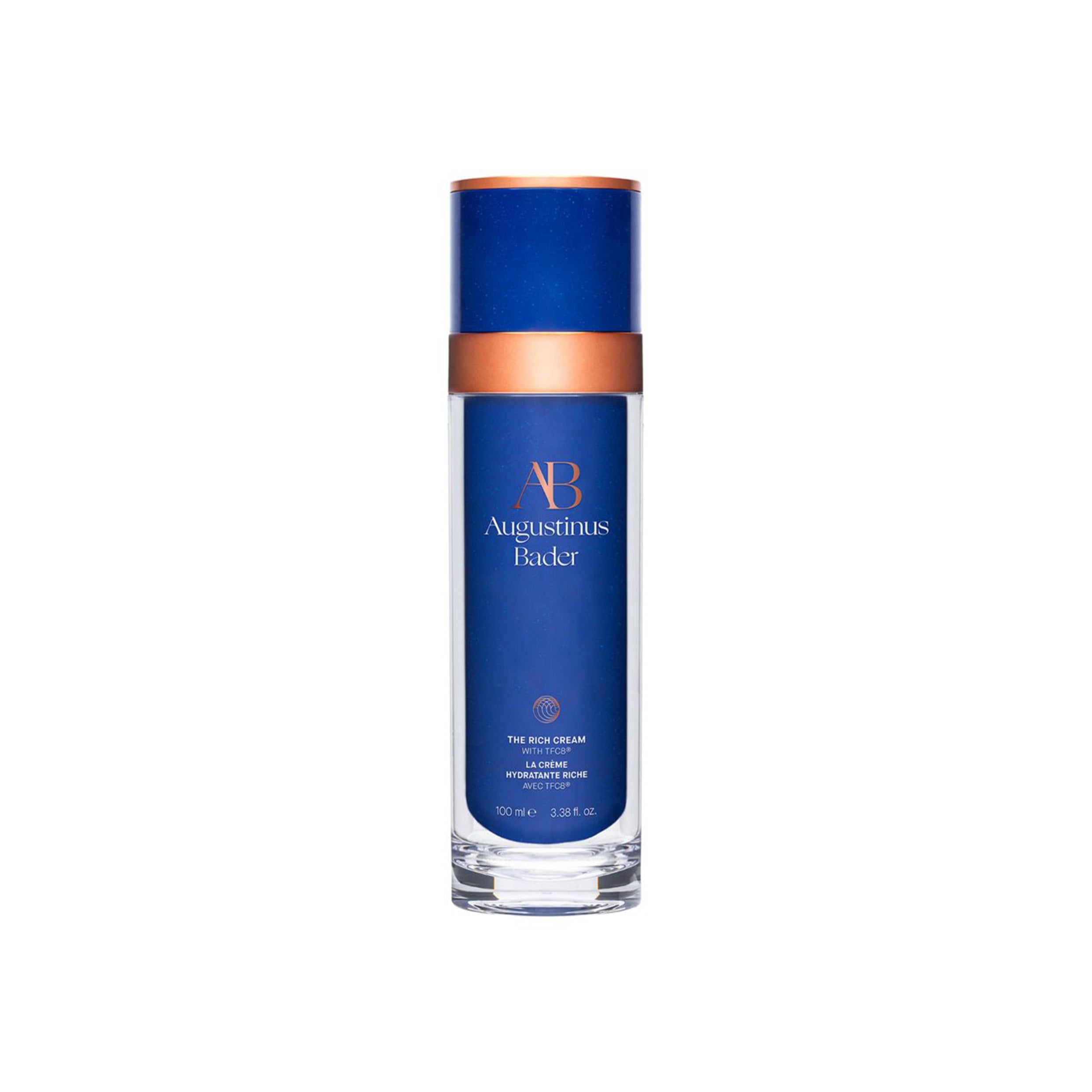 A blue and white bottle of Augustinus Bader The Rich Cream with a copper-colored cap.