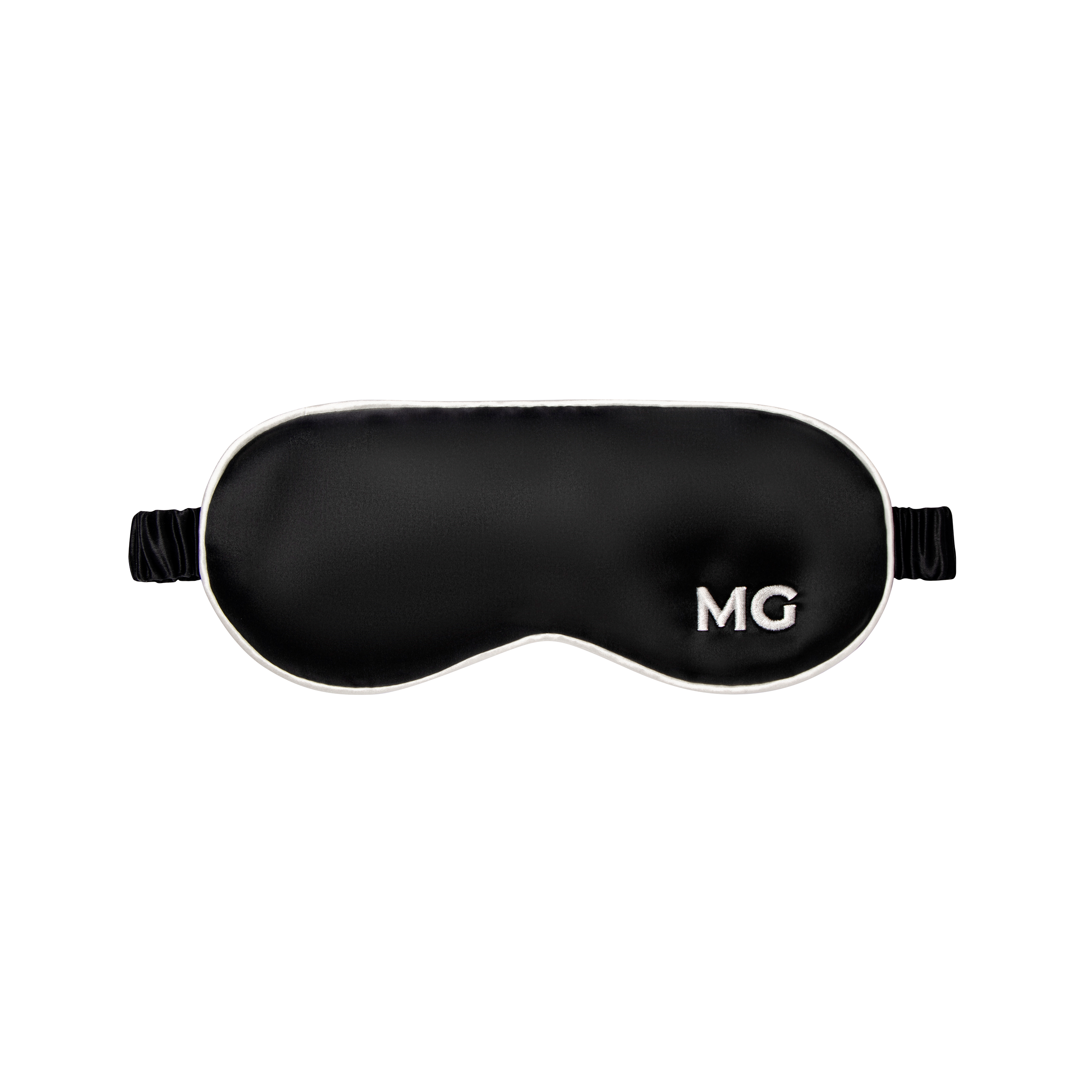 A black silk sleep mask with the initials 'MG' embroidered on the front.