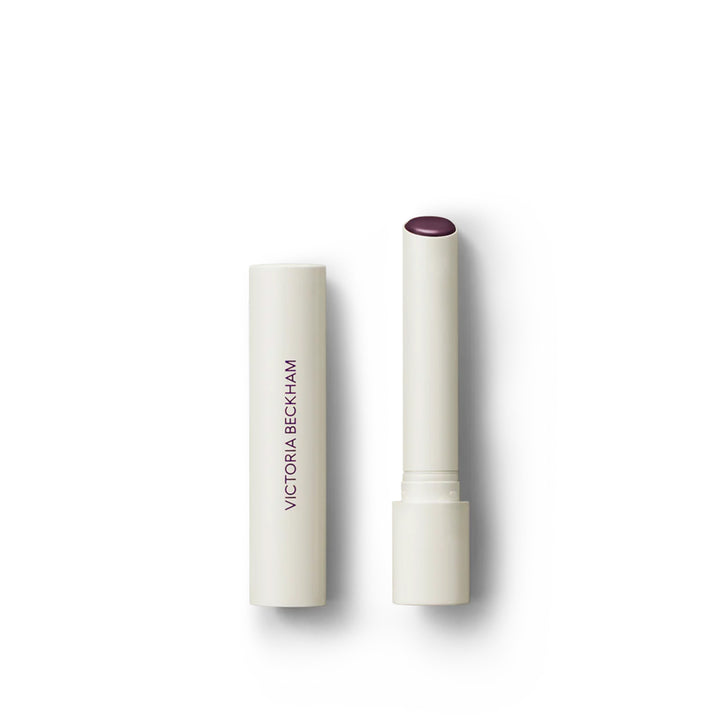 Victoria Beckham Beauty Posh Balm in Cassis, a lip balm with a white bullet dispenser and a sheer blackberry color.