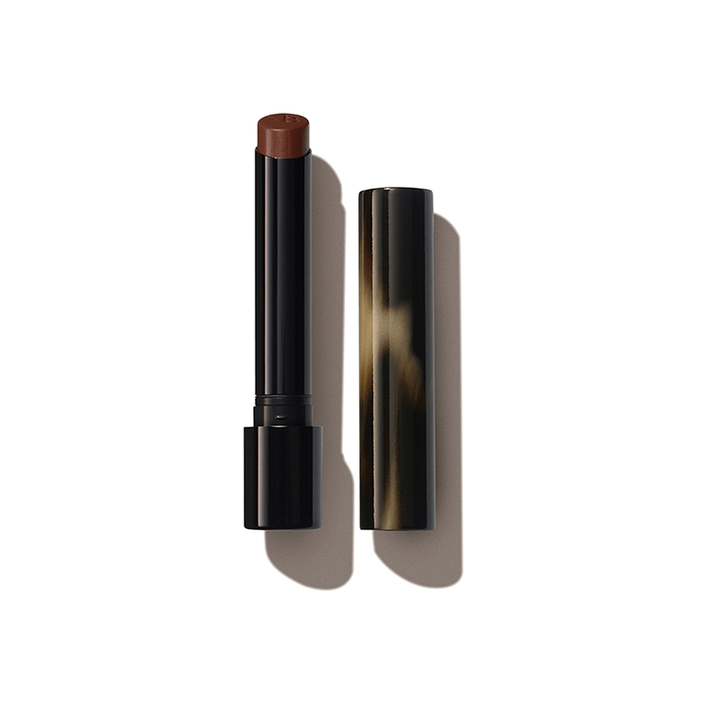 A Victoria Beckham Beauty Posh Lipstick in the shade Fringe, with the cap removed, showing a deep copper brown color.