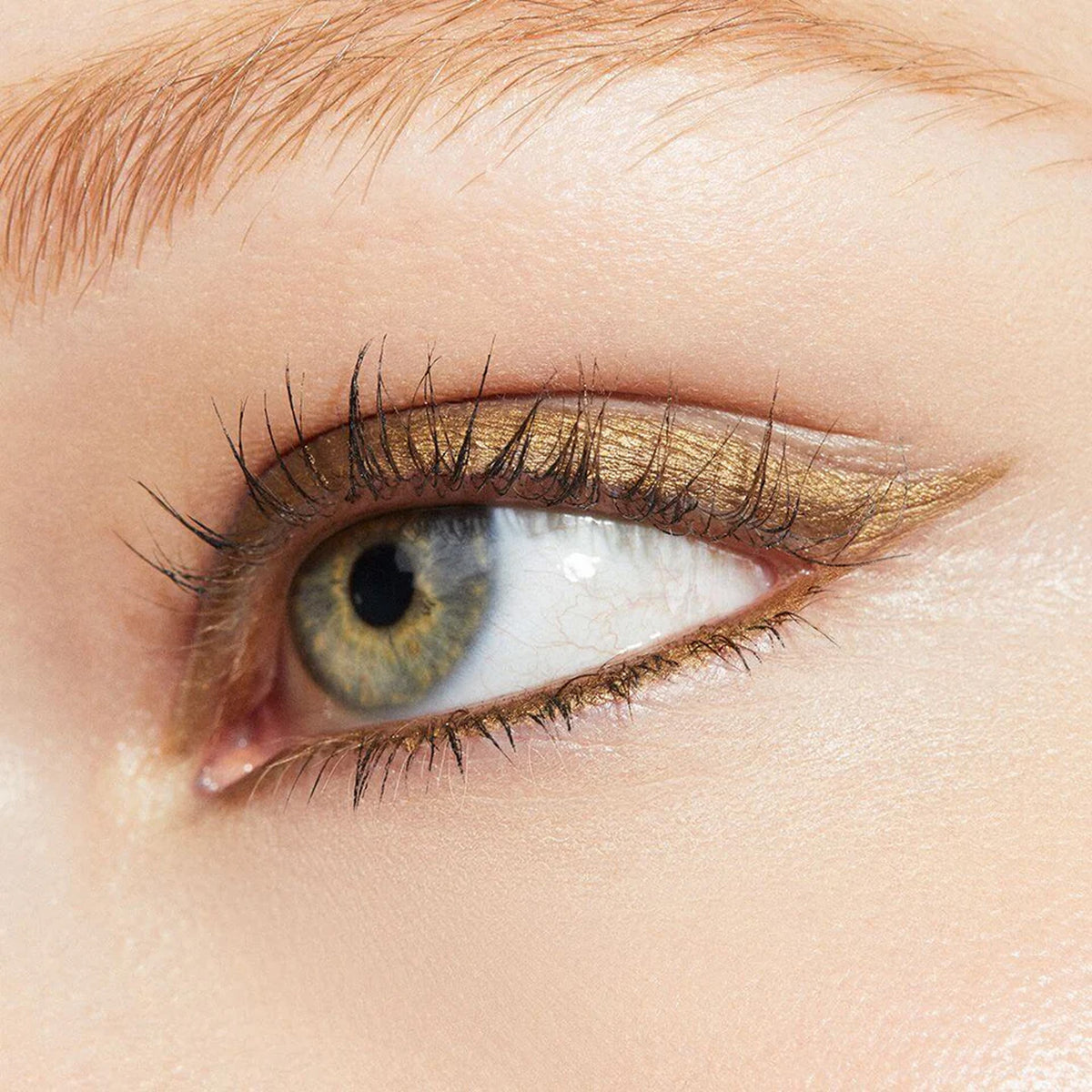 A close up image of an eye with gold coloured eyeliner applied to the eyelid.