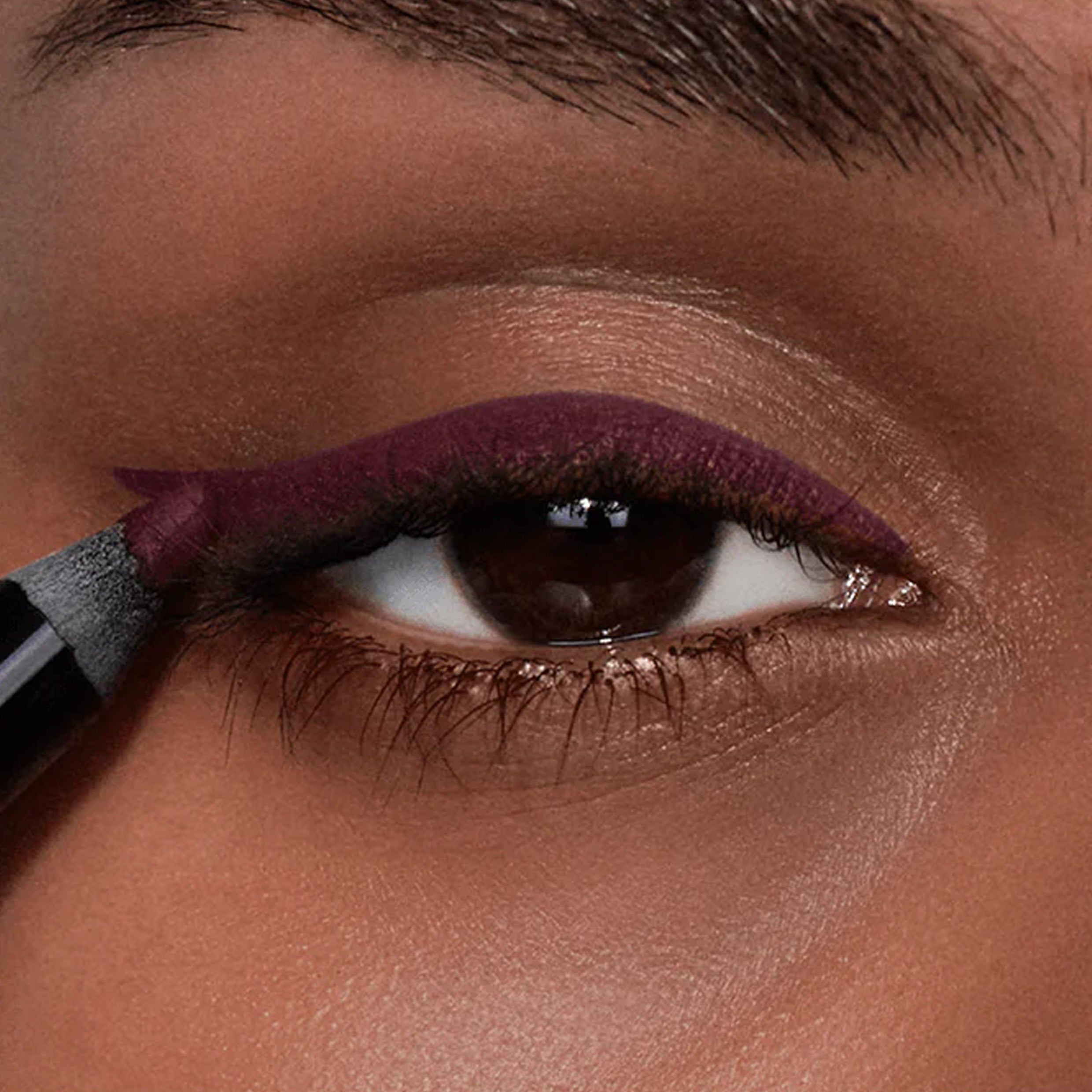 A close up image of an eye with eyeliner in a purple shade being applied to the eyelid.