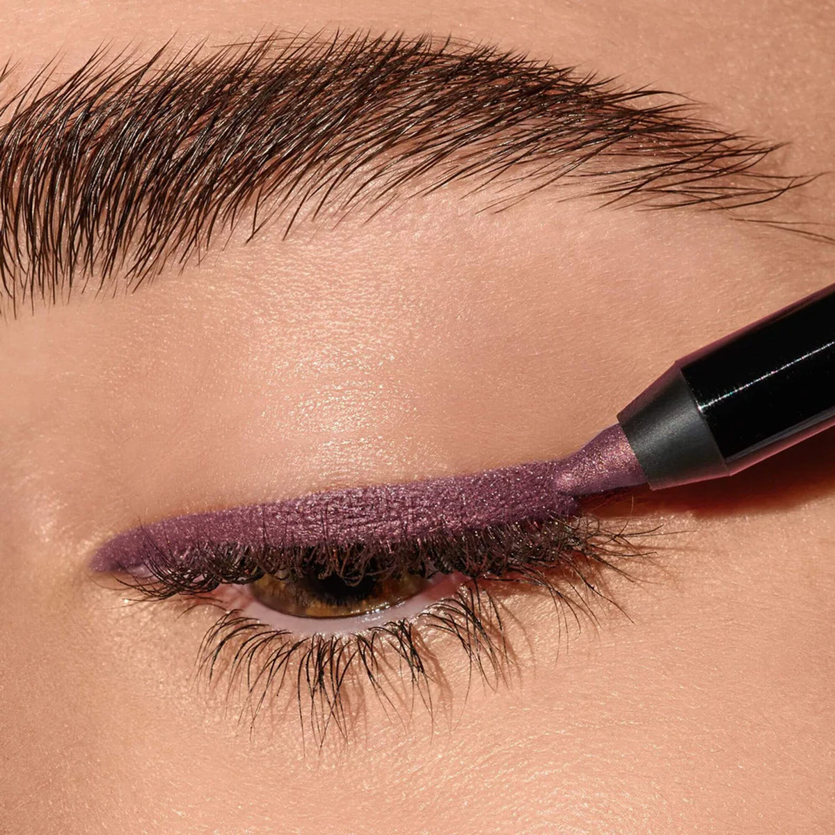 An eye lid with mauve eyeliner being applied with an eye pencil