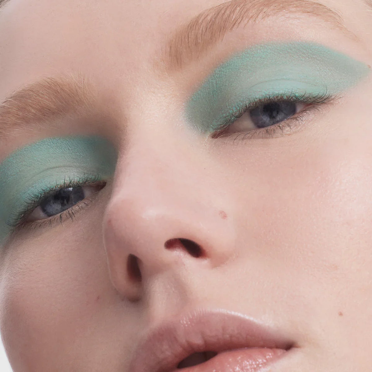A close up image of a face, with pastel green eyeliner applied to the eyelids.