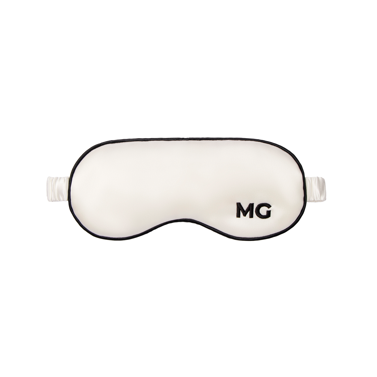 A white silk sleep mask with the initials 'MG' embroidered on the front.