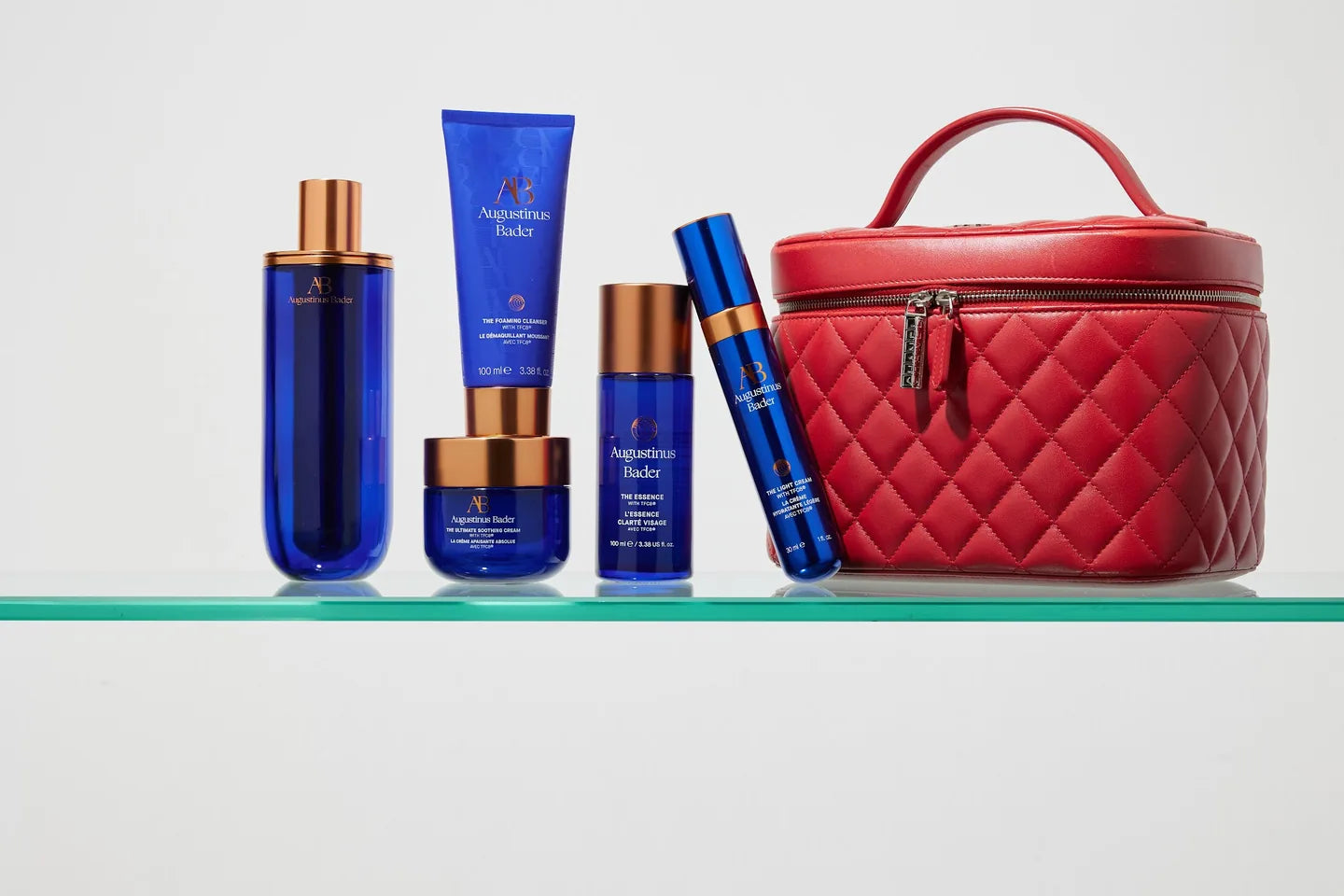 Augustinus Bader skincare arranged on a glass shelf with a red vanity case